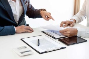 Two college-aged students review health insurance documents together at a kitchen table.